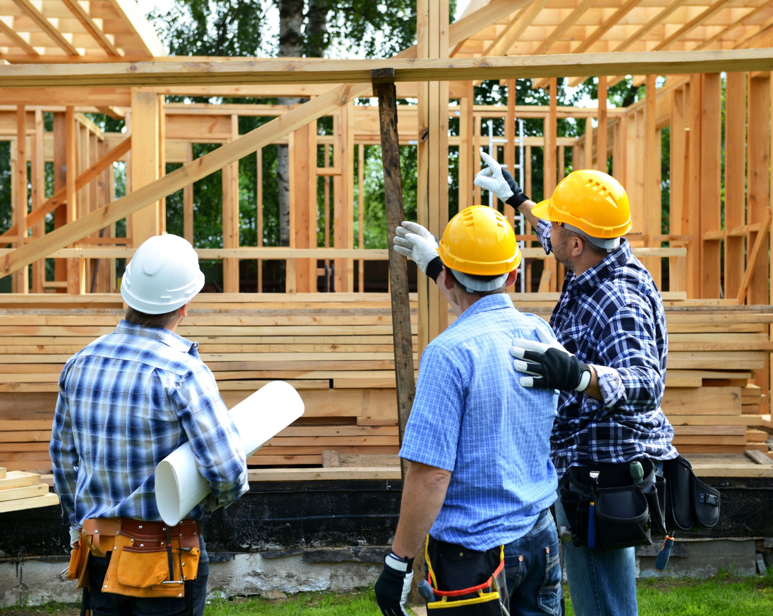 3 construction managers discuss plans in front of a home in development.