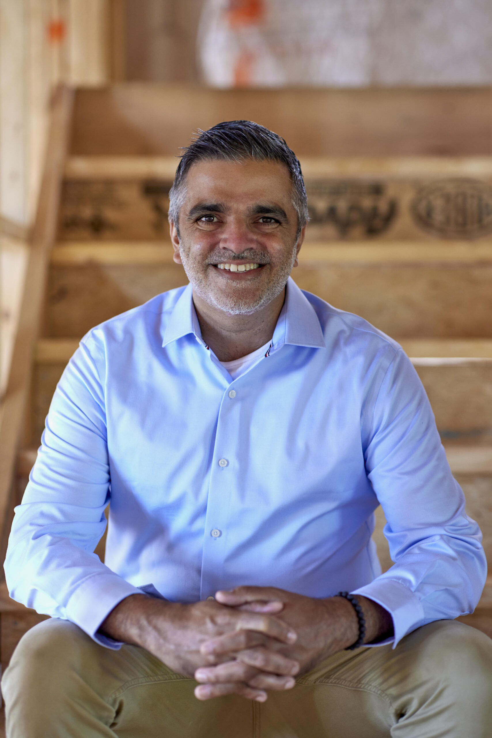 Headshot of Vicrum Puri, President and Co-Founder of August Homes, on a wooden staircase.